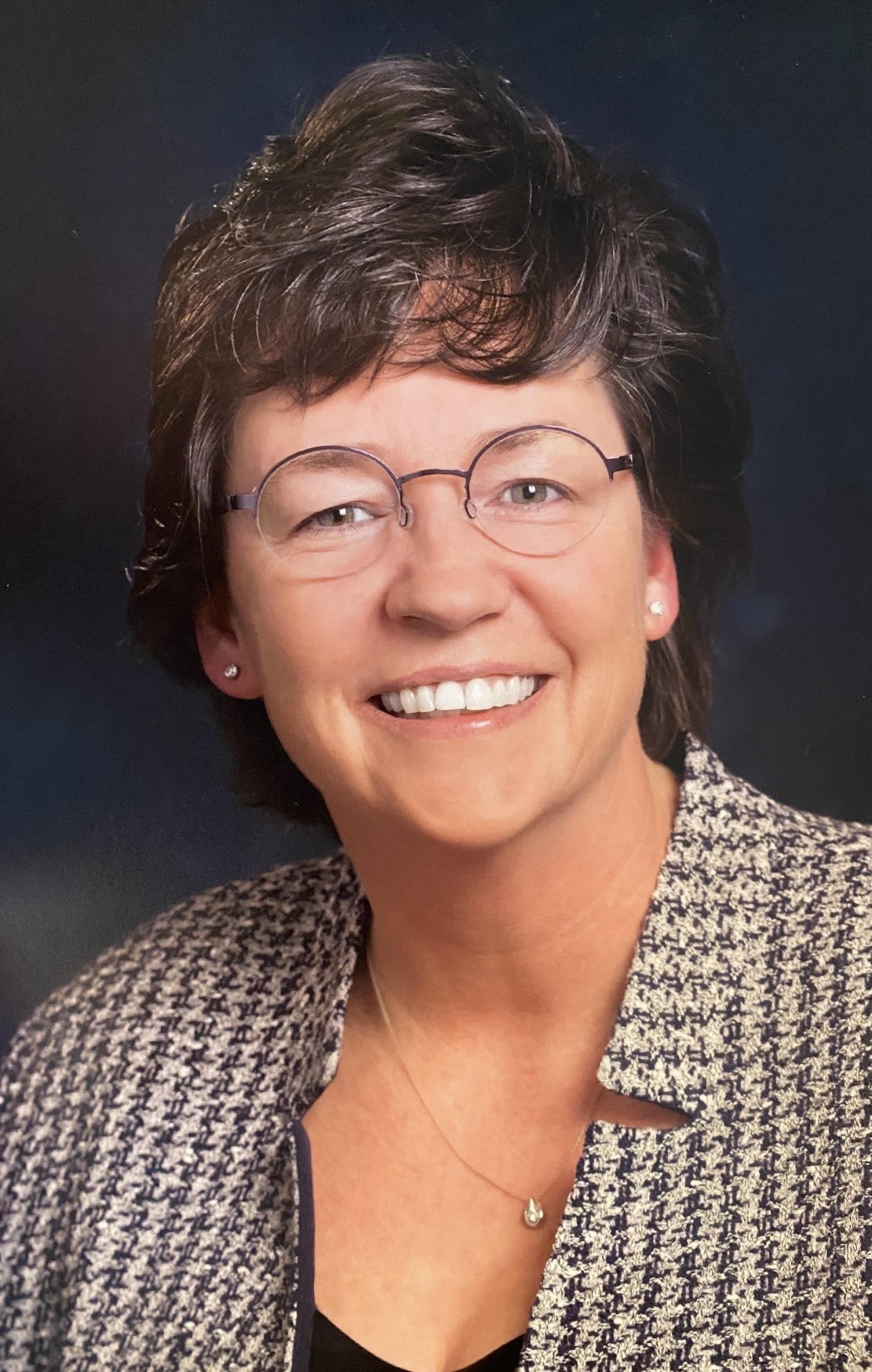 DeEtte R. Vasques, DO, MBA, gynecologic oncologist, smiling, wearing glasses and a houndstooth jacket, photographed against a dark blue background.